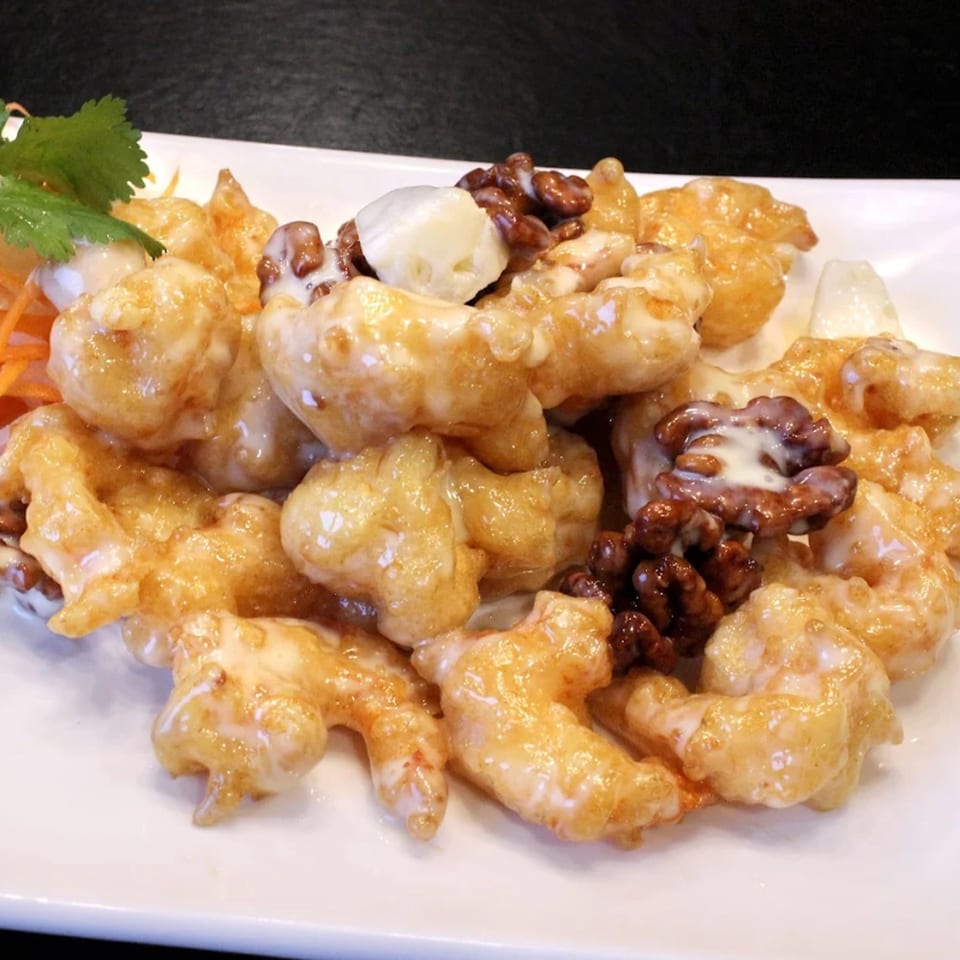 Honey walnut shrimp with creamy sauce, walnuts, and a garnish of cilantro and shredded carrots.