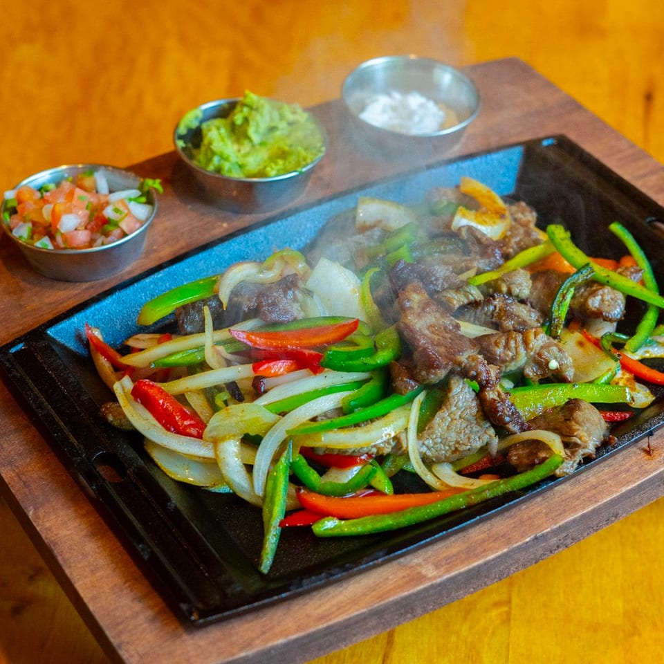 Sizzling fajitas with beef, colorful bell peppers, and onions, served with guacamole and salsa.