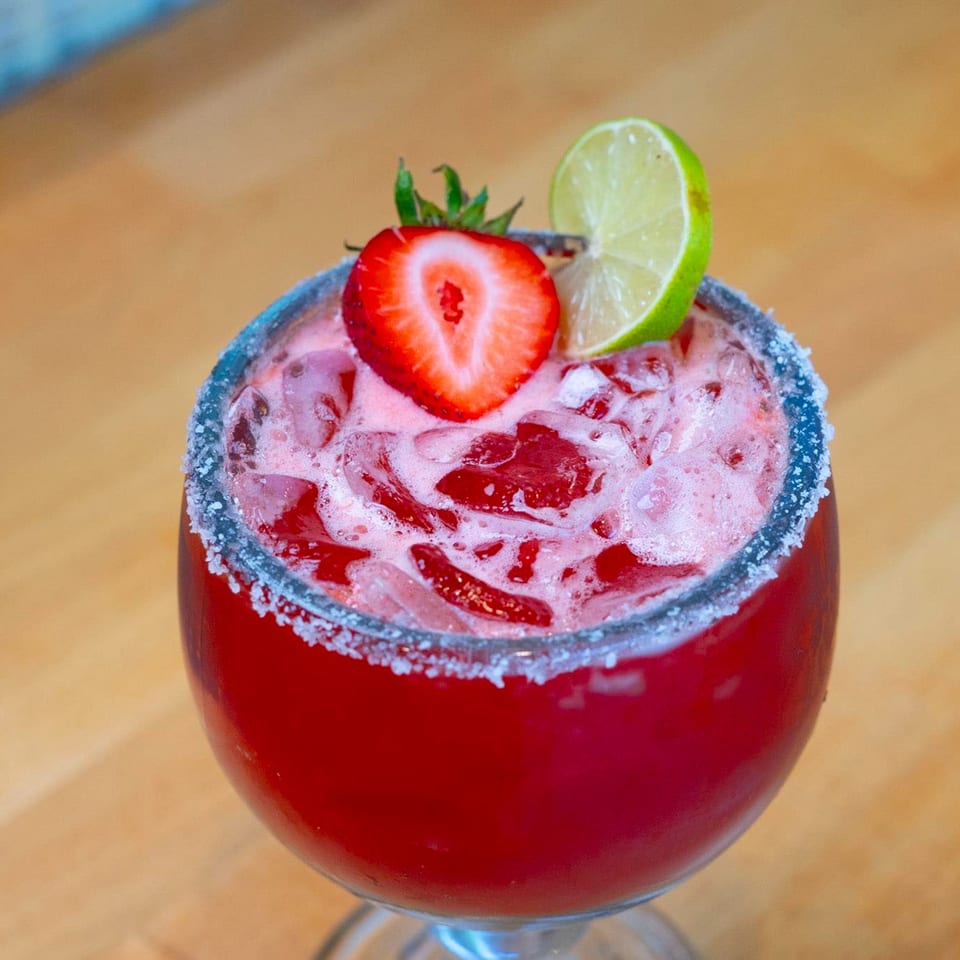 Vibrant red strawberry margarita with a salted rim, garnished with a strawberry and lime wedge.