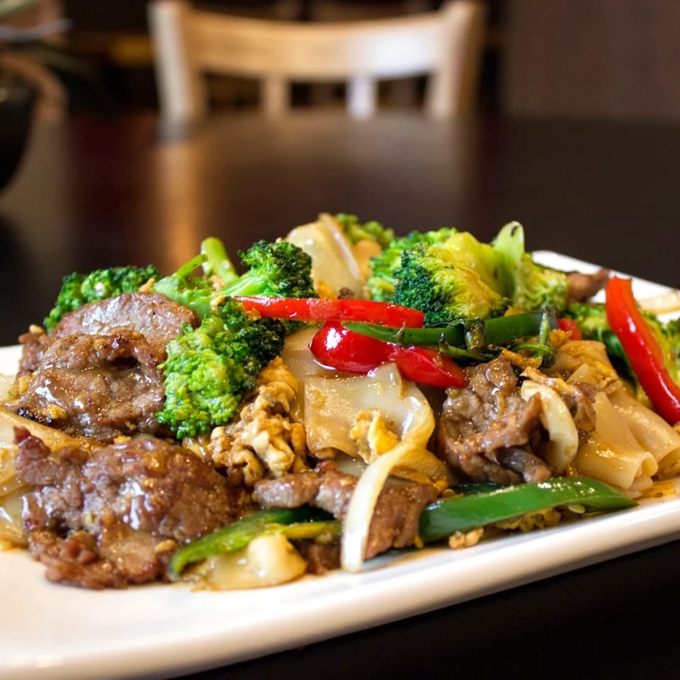 Asian stir-fry with beef, broccoli, red peppers, and noodles on a white plate.