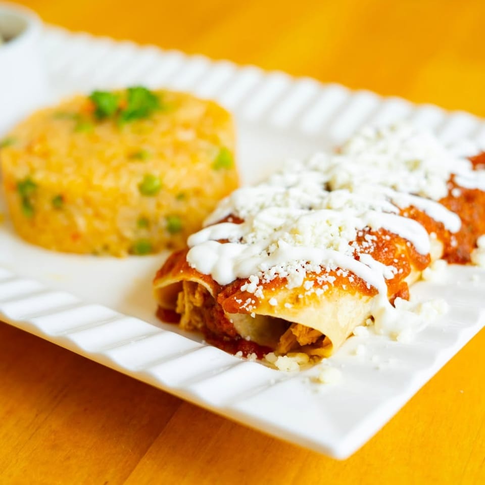 Three enchiladas topped with red sauce, sour cream, and cheese, served with a side of rice.