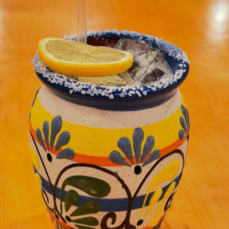 A colorful, hand-painted ceramic mug with a salted rim, filled with ice, a straw, and a lemon slice.