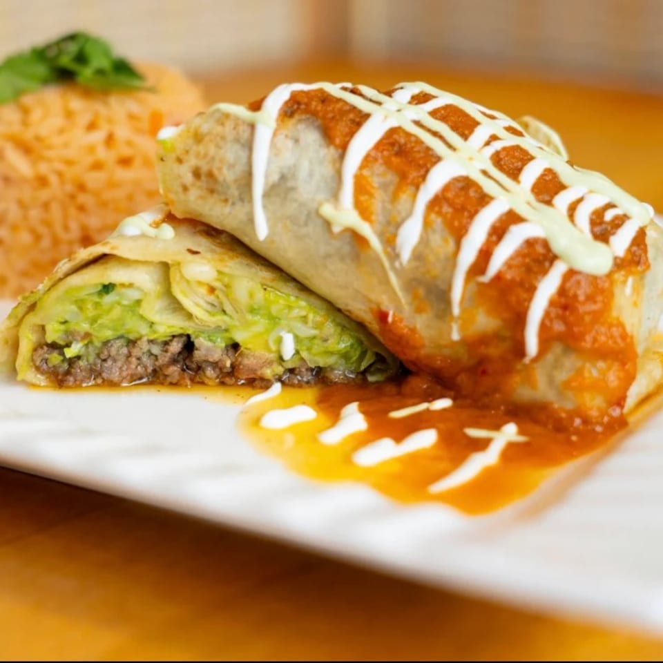 A Goji Y Agave burrito, cut in half, revealing meat and cabbage, drizzled with sauce and crema.