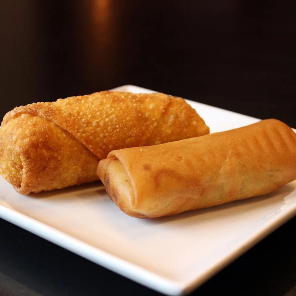 Two golden-brown, crispy egg rolls are presented on a white rectangular plate against a dark background.